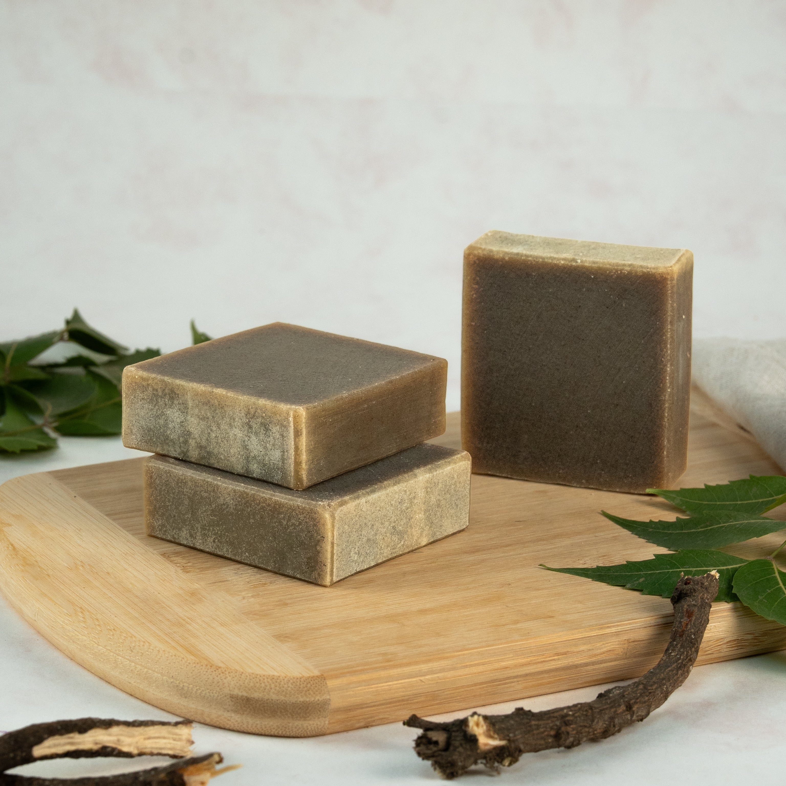 Three bars of soap on a wooden board with green leaves and branches on a light background