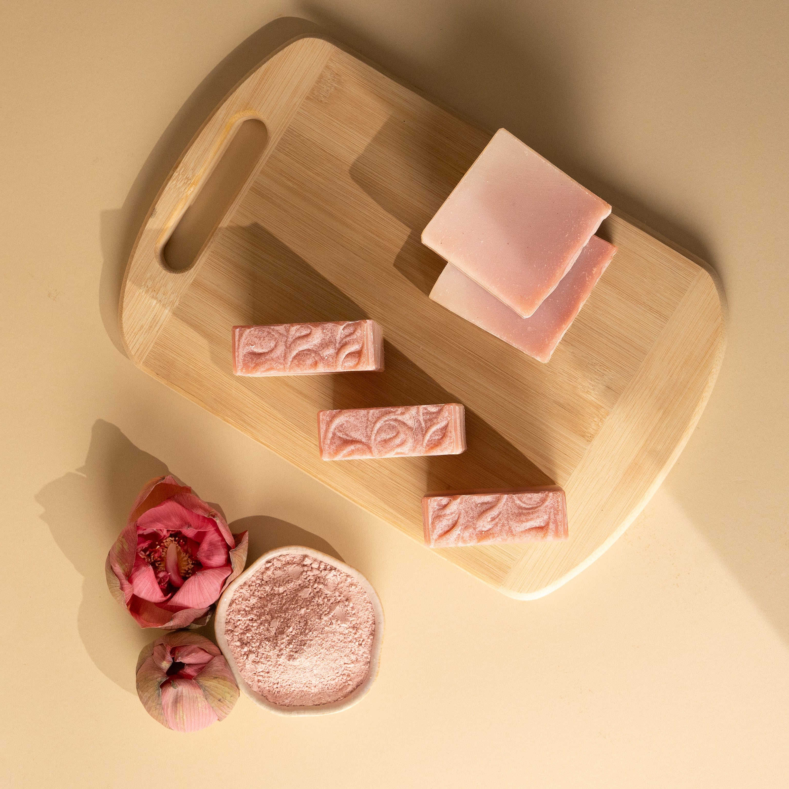 Pink soap bars on a wooden cutting board with a soft focus background