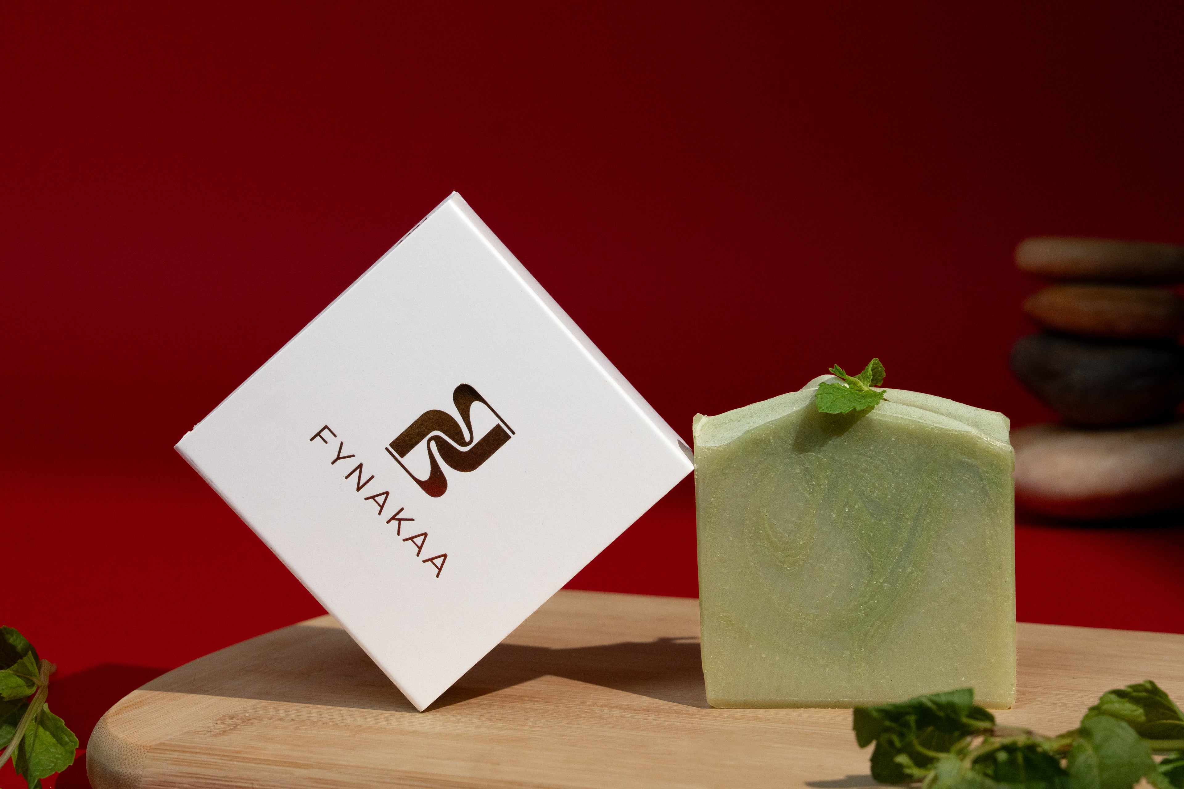 Green bar of soap with a white box featuring 'Fynakaa' logo on a wooden surface with a red background.
