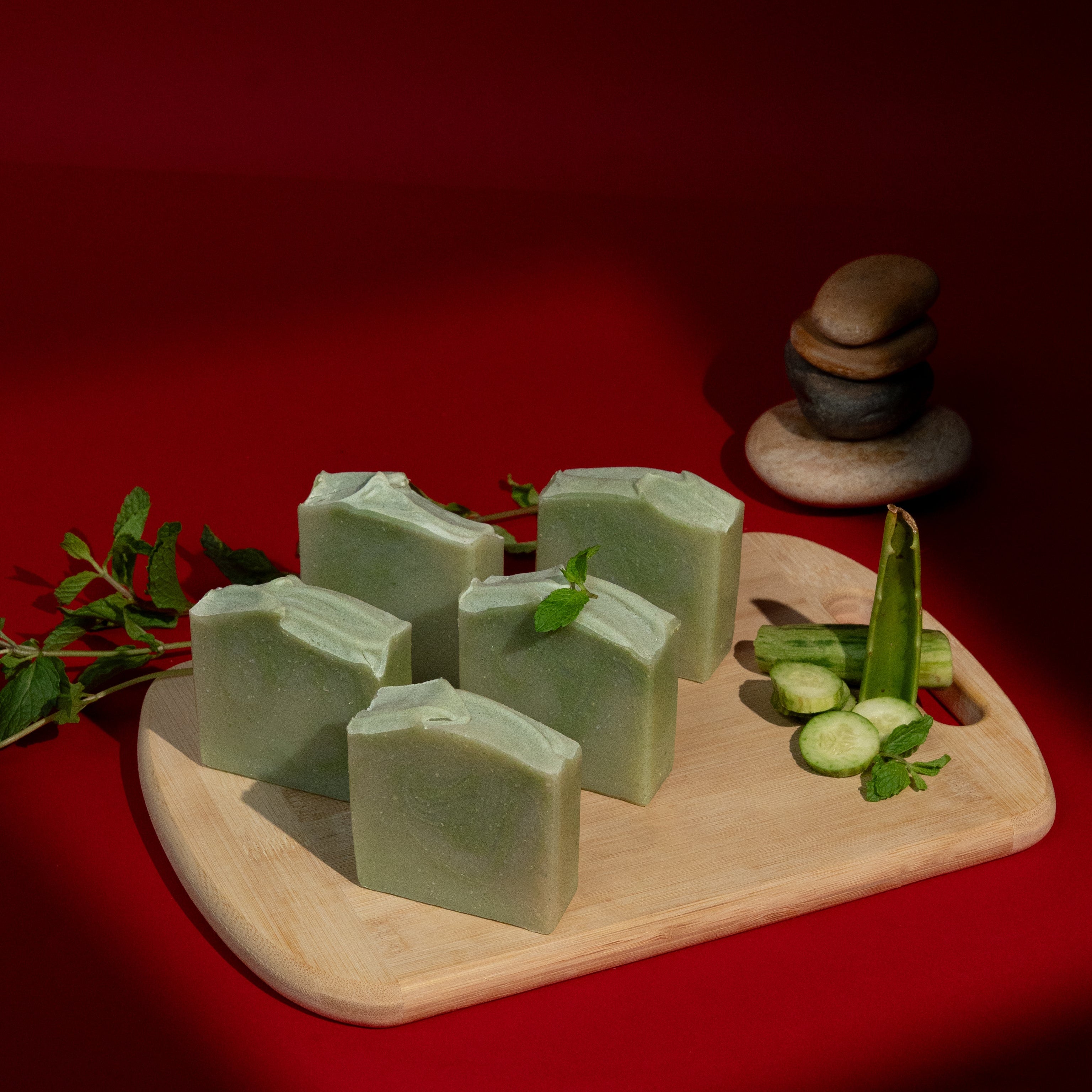 Green soap bars on a wooden board with green leaves against a red background