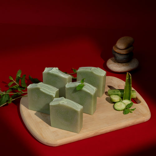 Green soap bars on a wooden board with green leaves against a red background