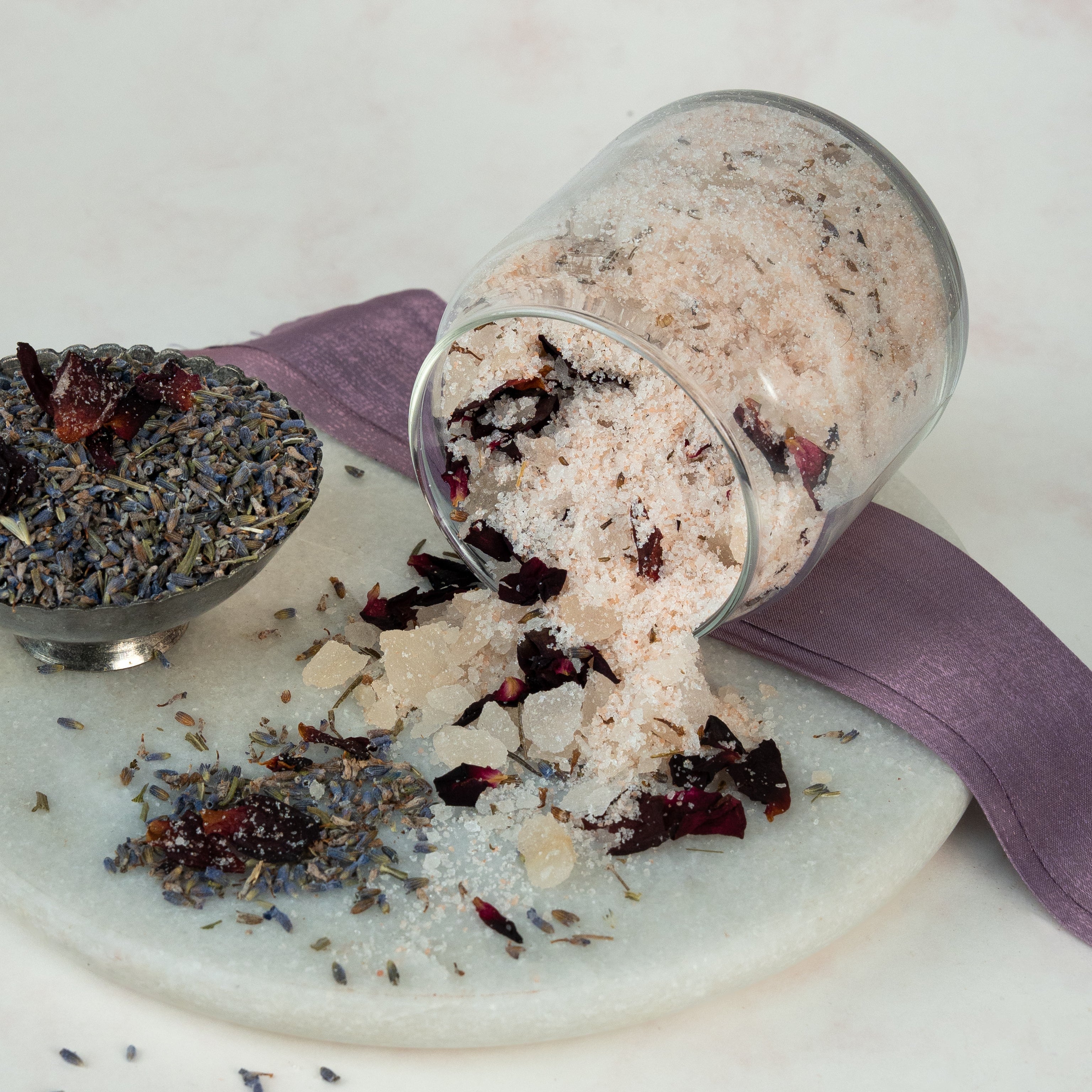 Glass jar of bath with dried rose and lavende on a white marble surface