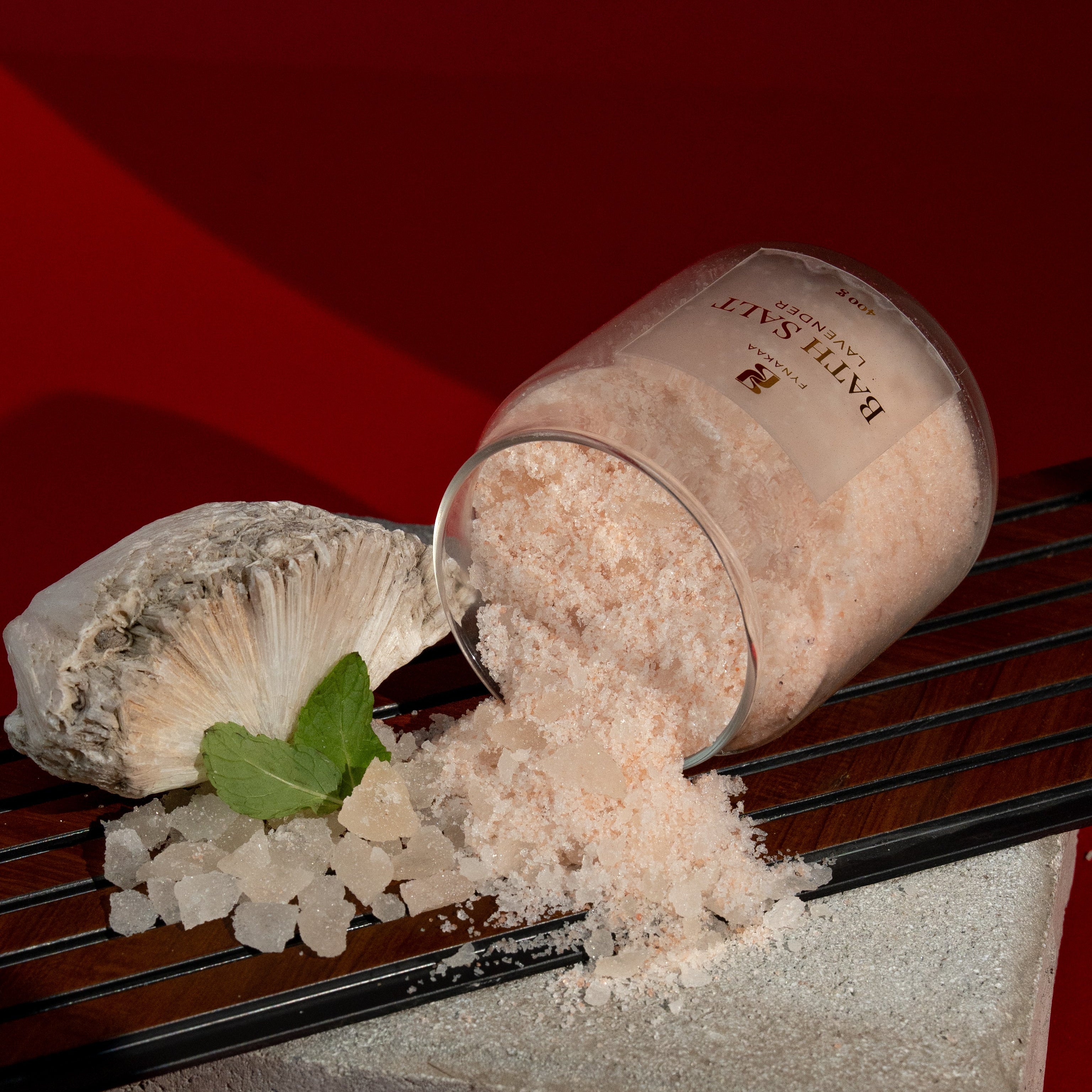 Open container of bath salt with a spoonful on a textured surface against a red background