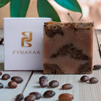 Fynakaa coffee-flavored soap with packaging on a wooden surface with coffee beans.