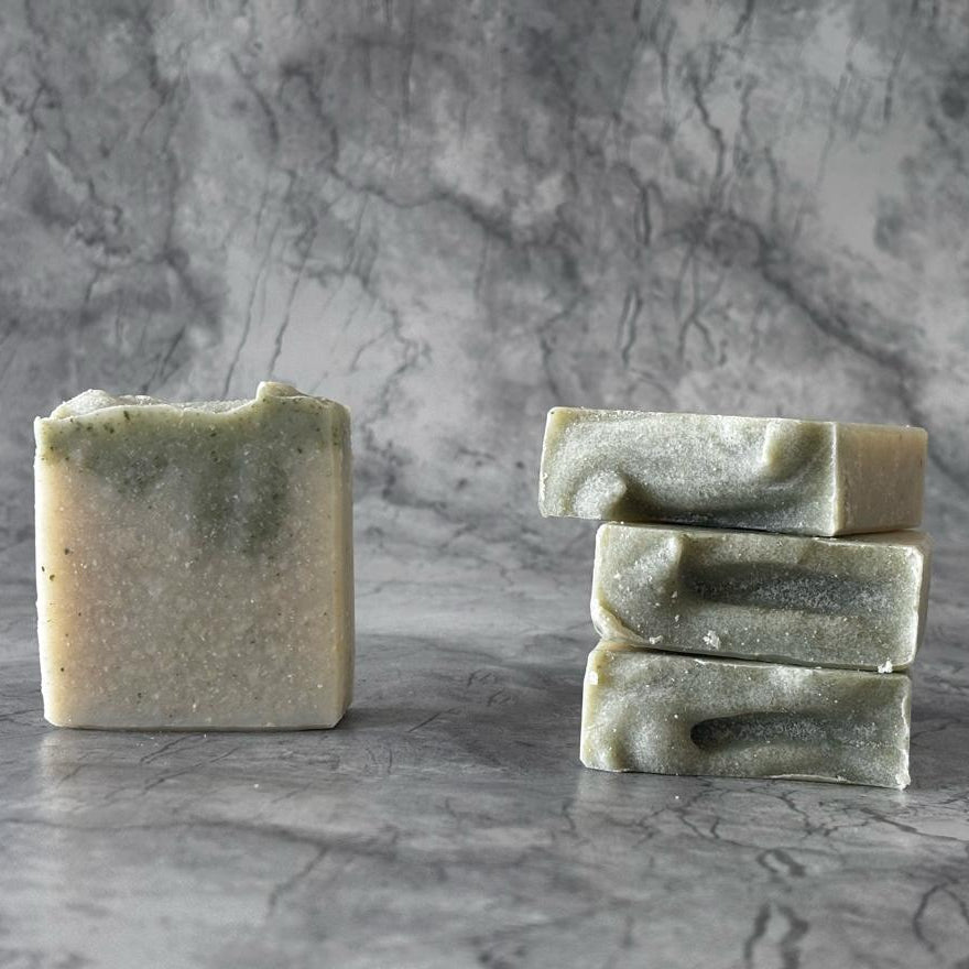 Three bars of green soap stacked on a gray marble surface with a gray marble background
