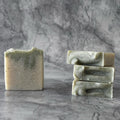 Three bars of green soap stacked on a gray marble surface with a gray marble background