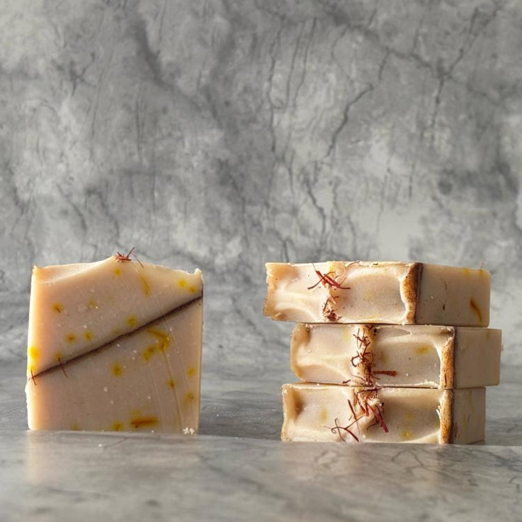 Three kesar chandan soap bars stacked on a marble surface with a gray marble background