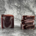 Handcrafted soap bars with a dark pin color and natural patterns, displayed on a textured background.