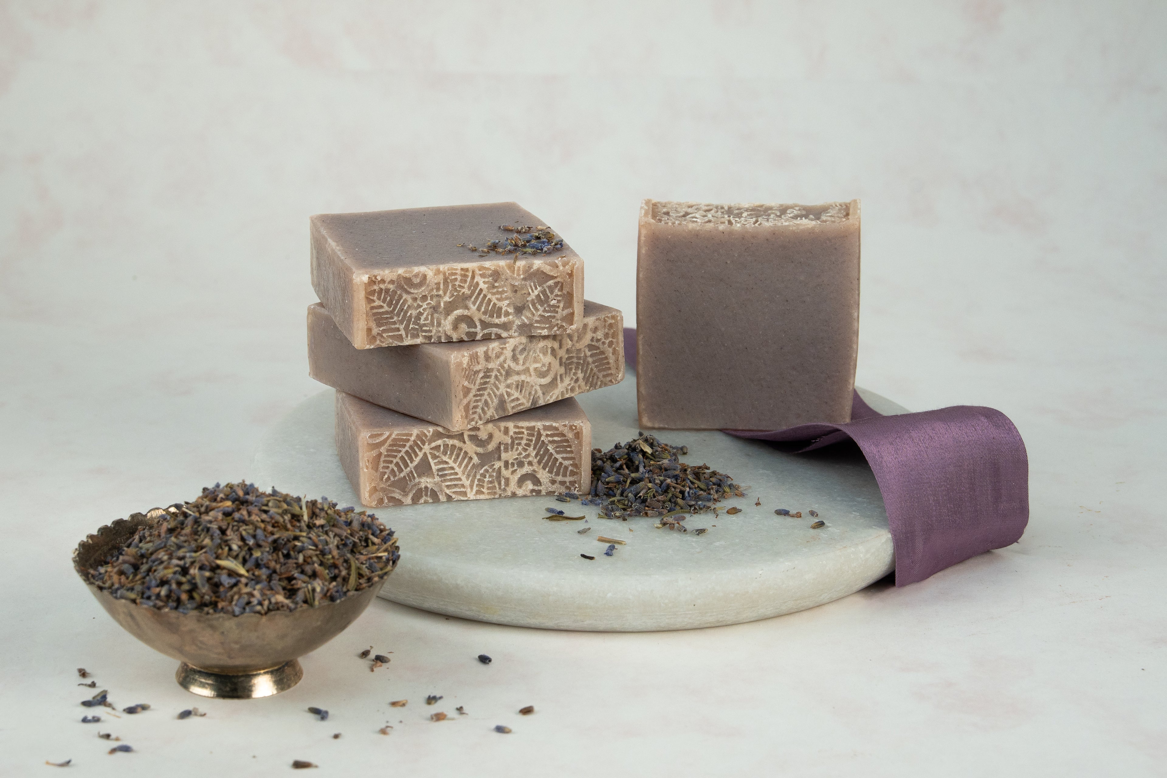 Handmade soap bars with a decorative design on a white surface with lavender flowers.