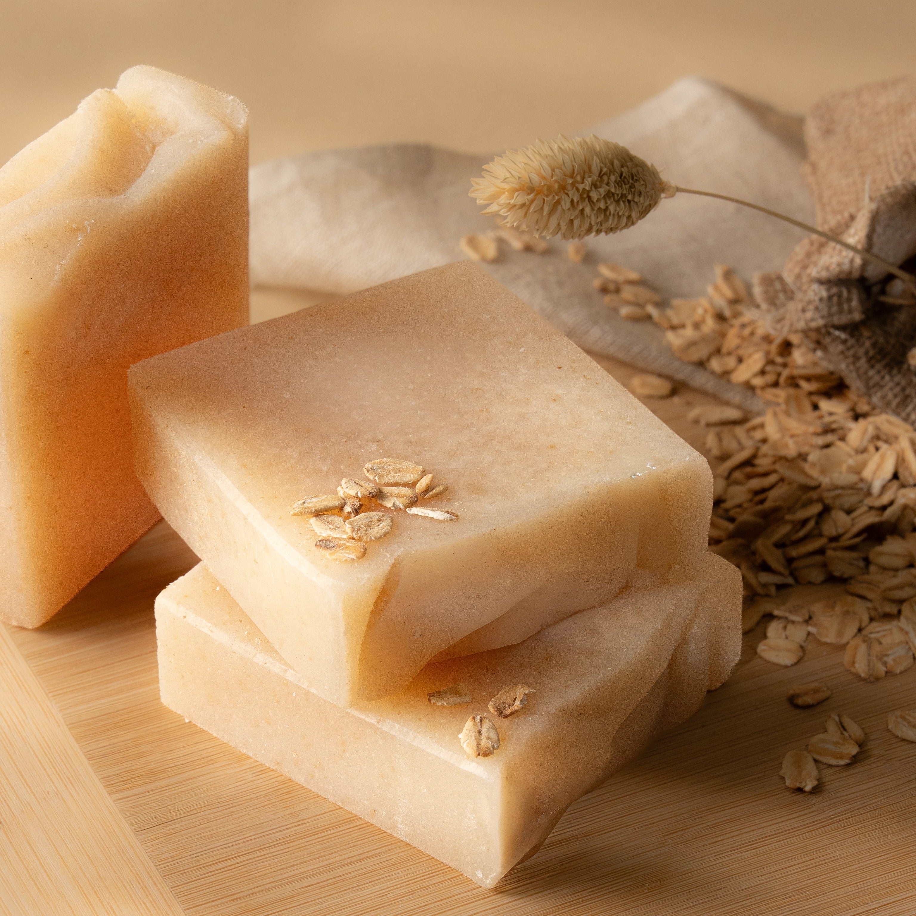 Three bars of soap on a wooden surface with oats around