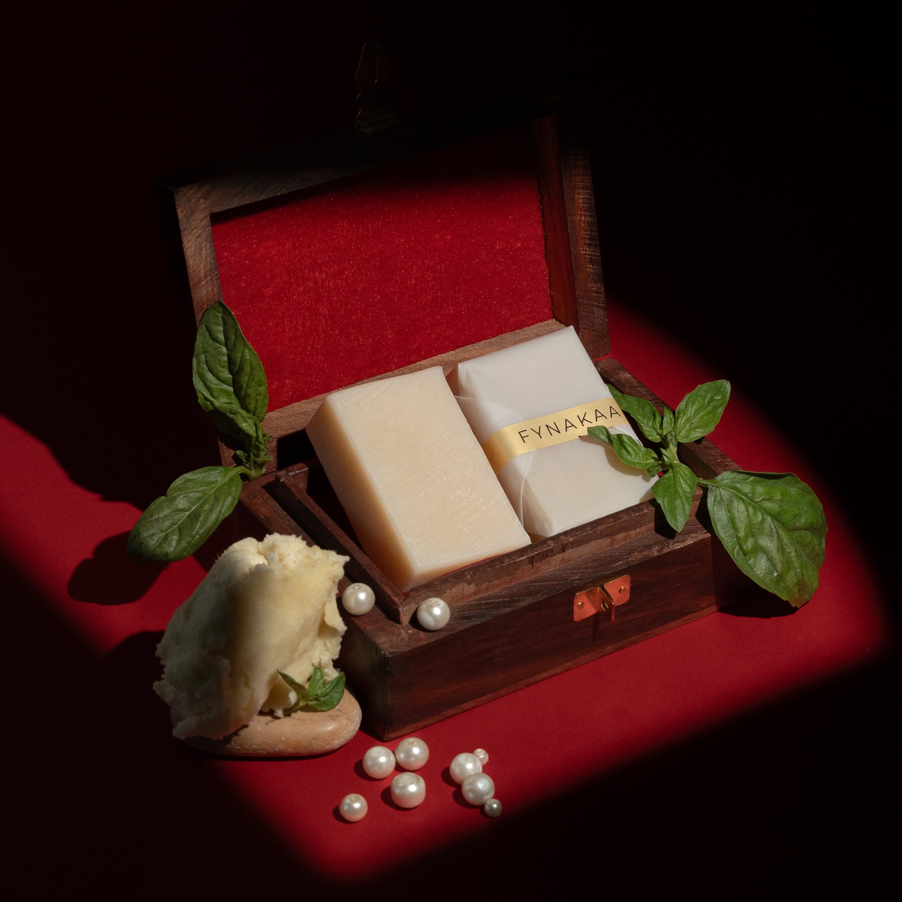 Wooden box with two beige soaps a red surface with green leaves and pearls