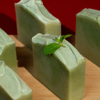 Green soap bars with a mint leaf on a wooden surface against a red background